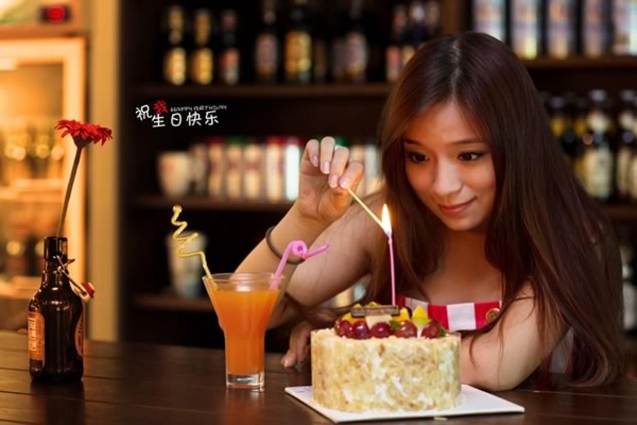 几位穿红色条纹衣裤的姑娘在酒吧生日聚会，过生日的姑娘要了一杯橙汁，拿着另一只蜡烛，用已经插在生日蛋糕上的点着的蜡烛引燃