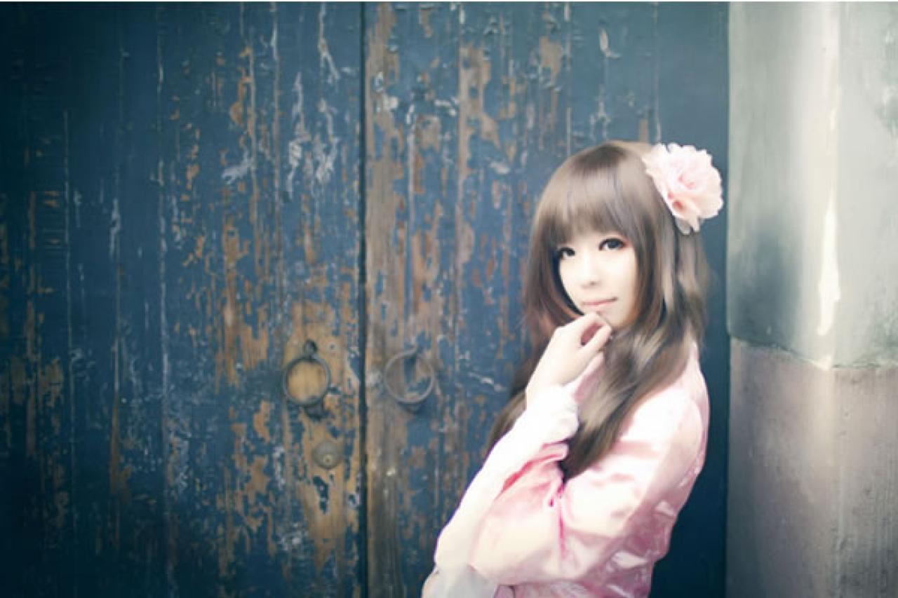 季_凋葬穿着粉衣扮演湾娘轻抚着下巴，在蓝的有点褪色的老式双开木门旁的侧身照