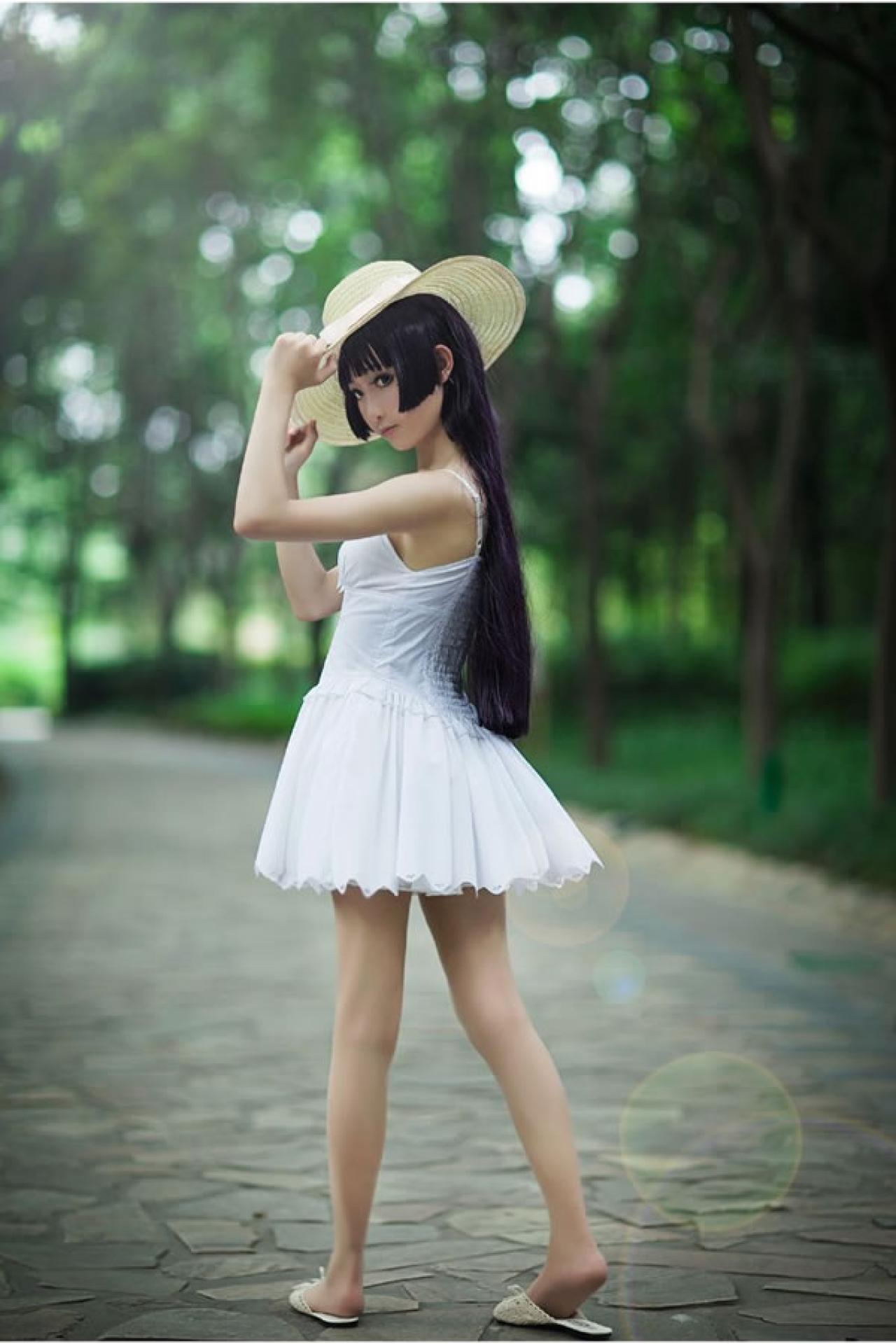 镜祭穿着白色连衣短裙扮演五更琉璃白猫，戴着太阳帽，双手拉着太阳帽帽沿，在石子铺成的小路上，走着回头看过来