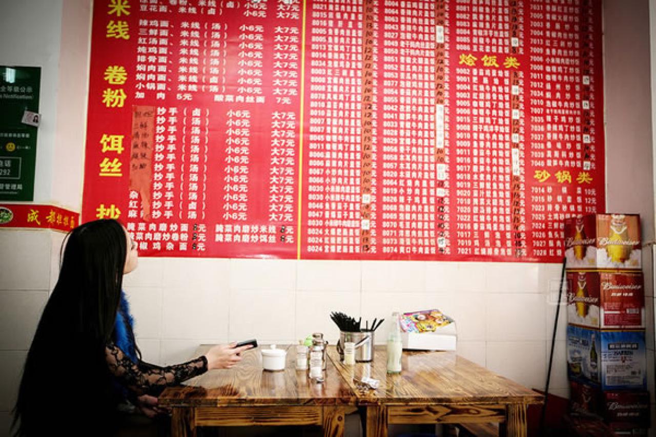 90后Showgirl王可欣正在北京的一家小吃店里看着墙上的红布菜单