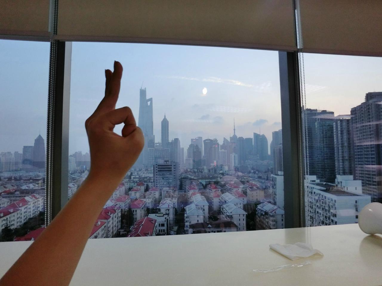 猫咪的小主人尾喵在落地窗前，比照太阳，作了一个猫耳手势