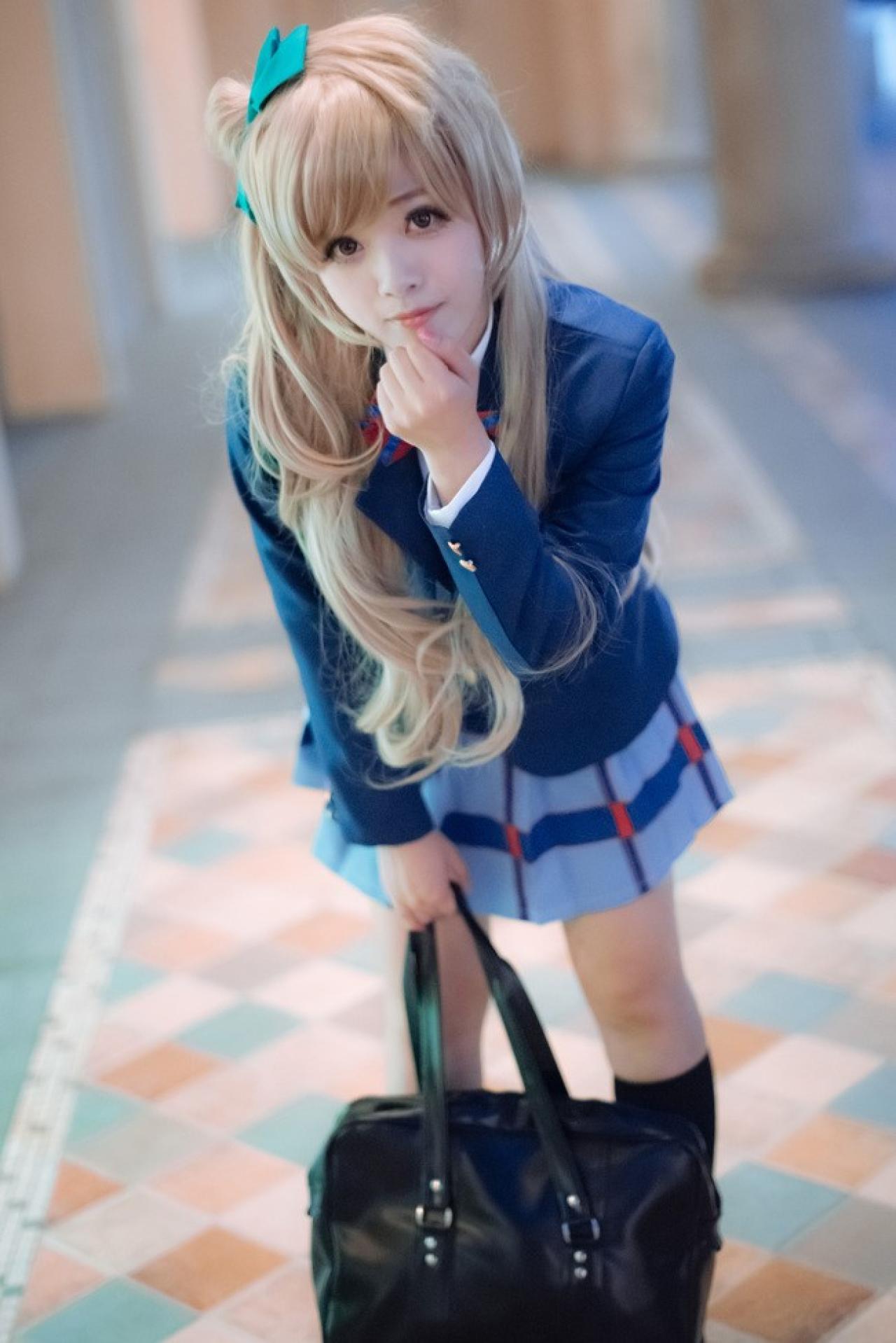 四月www扮演南小鸟右手提着包，左手捏着下巴，附身的姿势