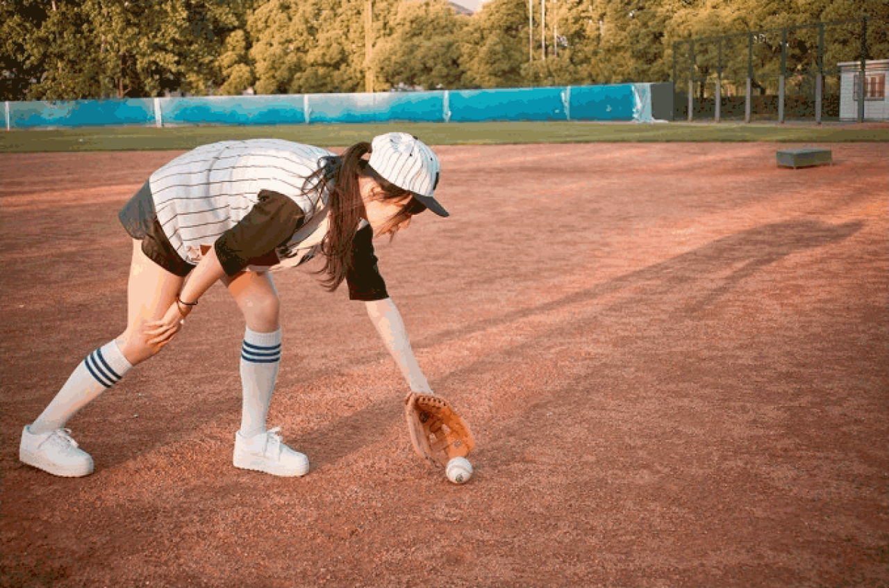 馋宝宝弯腰，右手扶着膝盖，左手去捡掉在地上的棒球