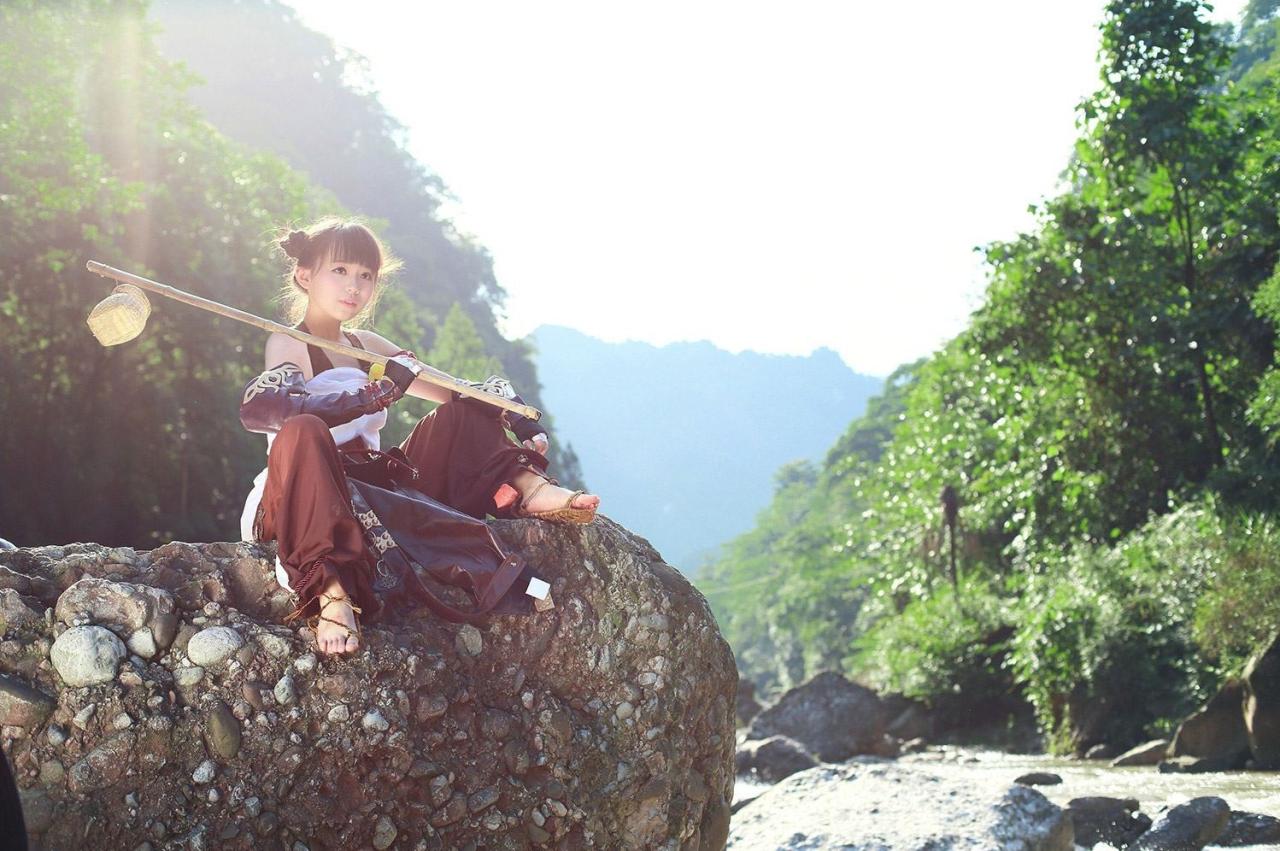 修老虎扮演丐帮萝莉拿着吊着半个罐子的竹竿坐在石头上左侧视角照