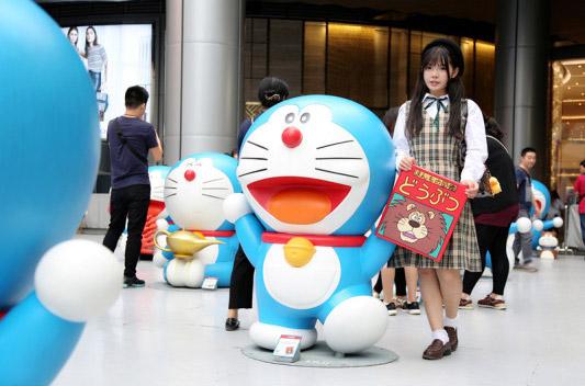 彩虹姐姐拿着红色封面和双手抬起的哆啦A梦在一起