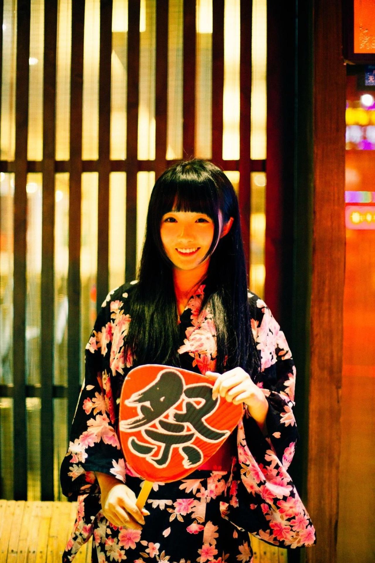 小炉子右手持扇，左手捏着扇子一角微笑站立