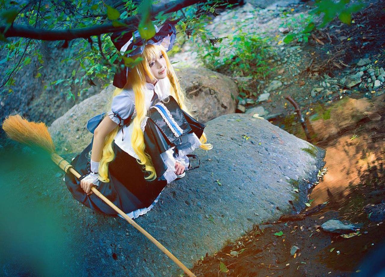 雨扮演雾雨魔理沙，右手抓着扫把，左手扣在鞋子上，蹲坐在水边的石头上