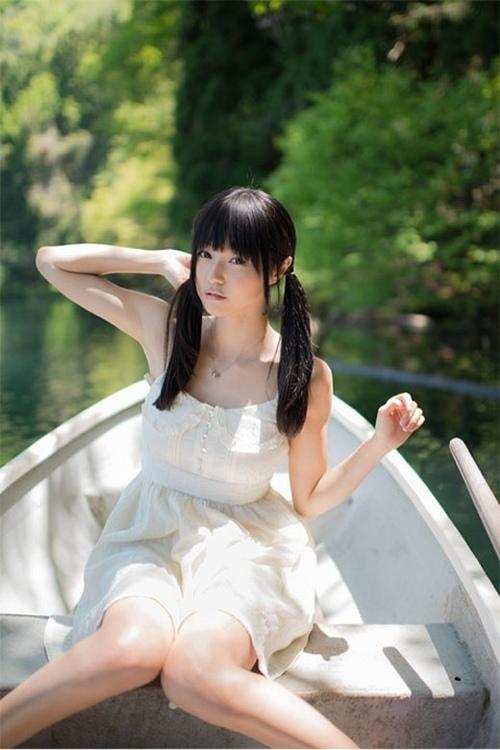 小出友华坐在床头，左臂抬起，右手轻抚马尾