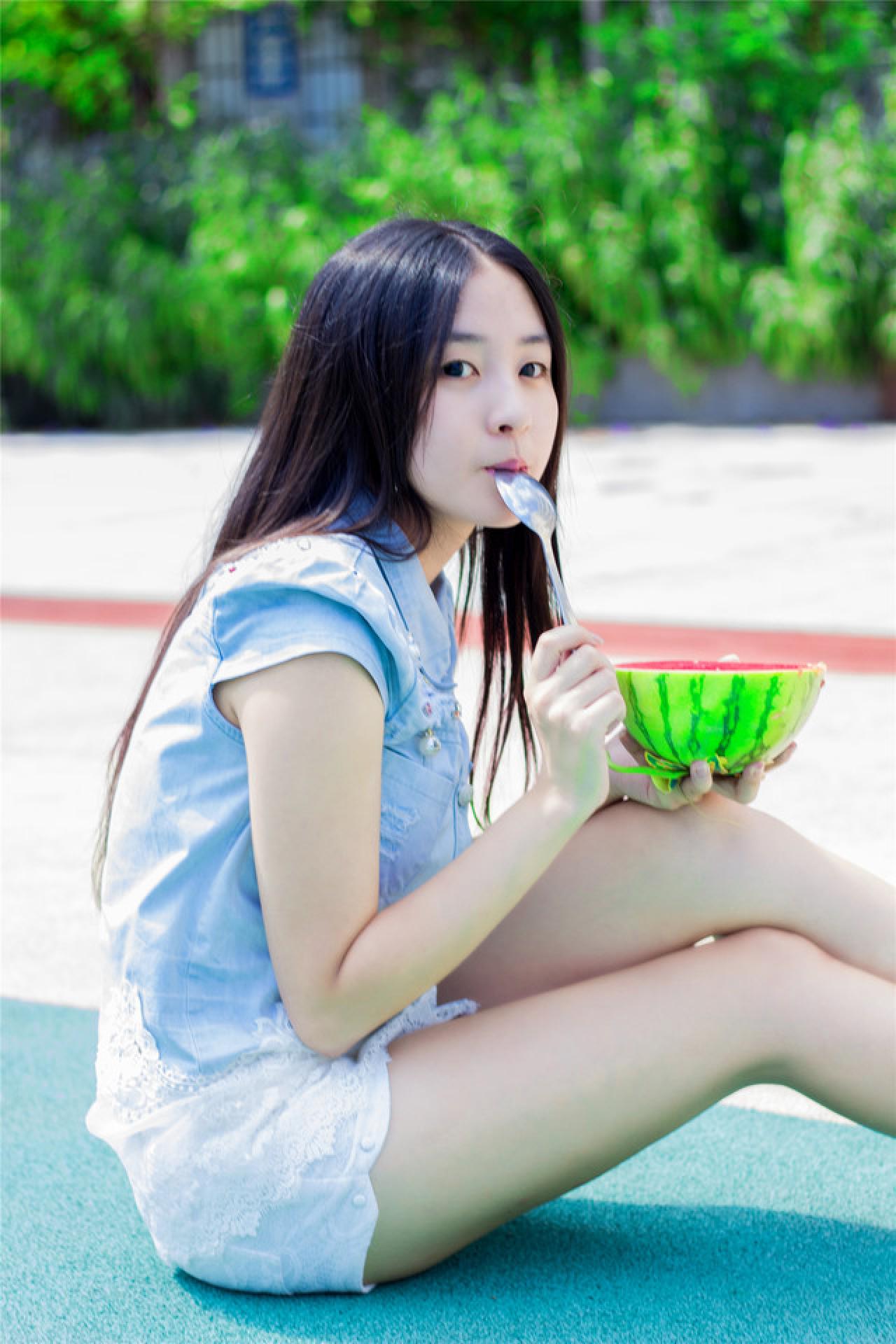 陈婕坐在操场，左手端着西瓜，右手拿着勺子咬在嘴里