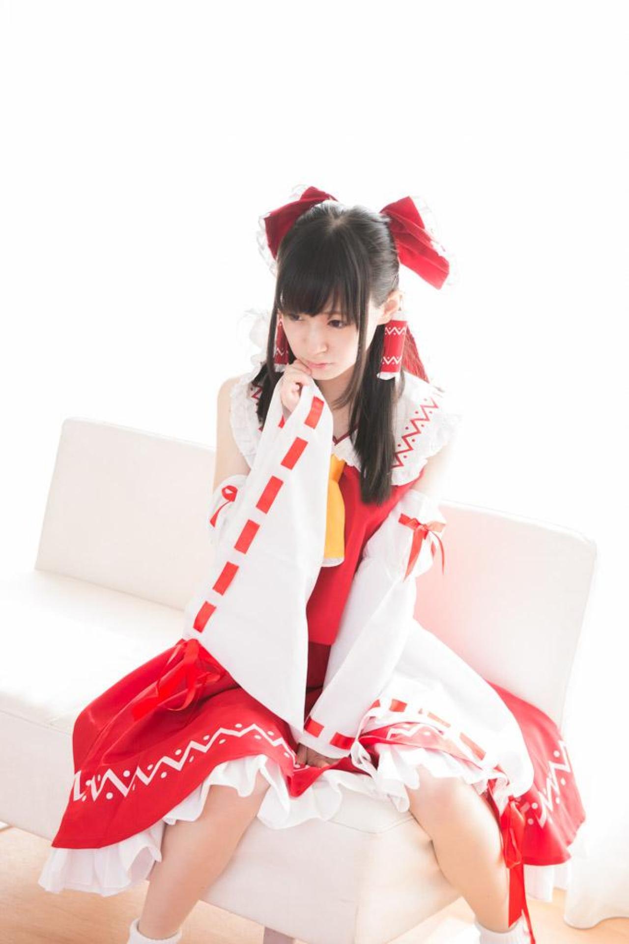 近衛りこ扮博丽灵梦坐在沙发，抬起右手轻扶脸颊，左手撑在裙摆上