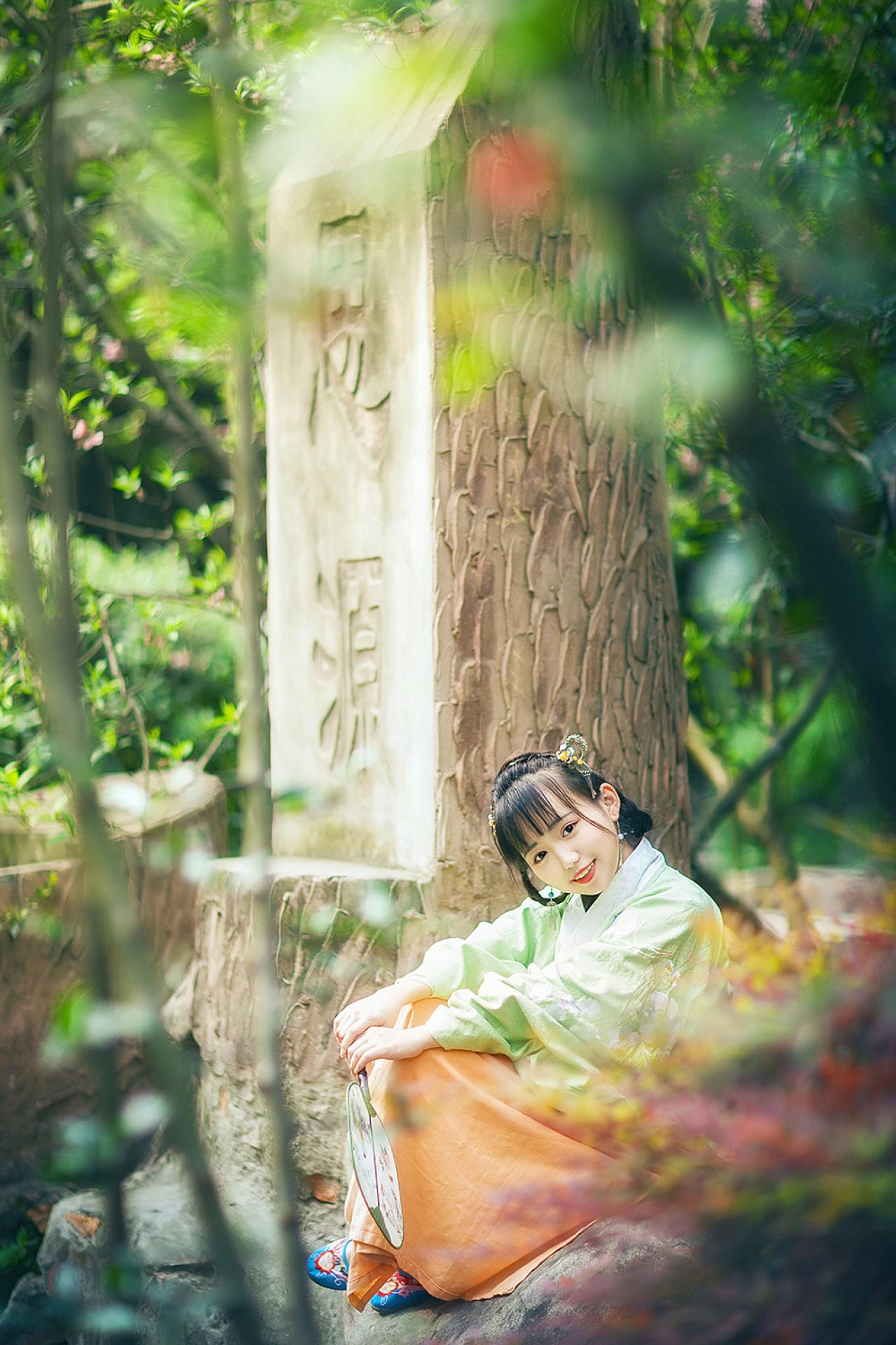 修老虎双手搭在膝盖上，侧身坐在树干旁，回眸看镜头