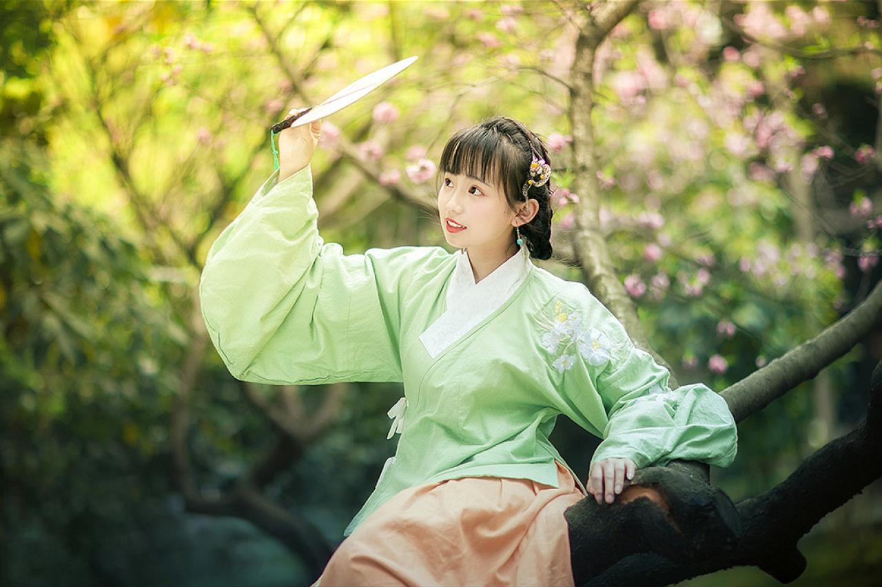 修老虎坐在梅花树干上，右手持扇顺着目光抬起