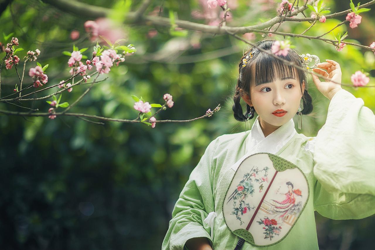 梅花枝条下，修老虎右手持扇站立，左手轻扶发簪