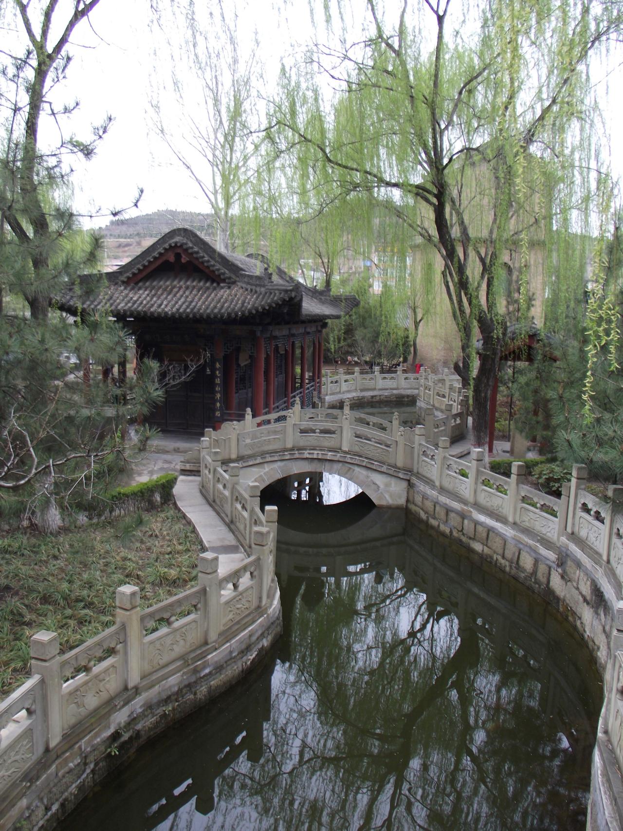 柳树下，曲折的溪水穿过拱桥，围绕凉亭流入湖中的素材