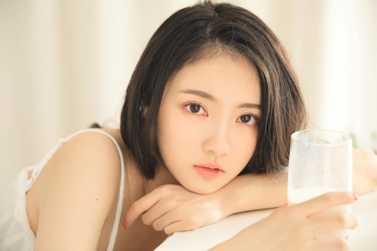 少女趴在桌面，右手握着牛奶杯