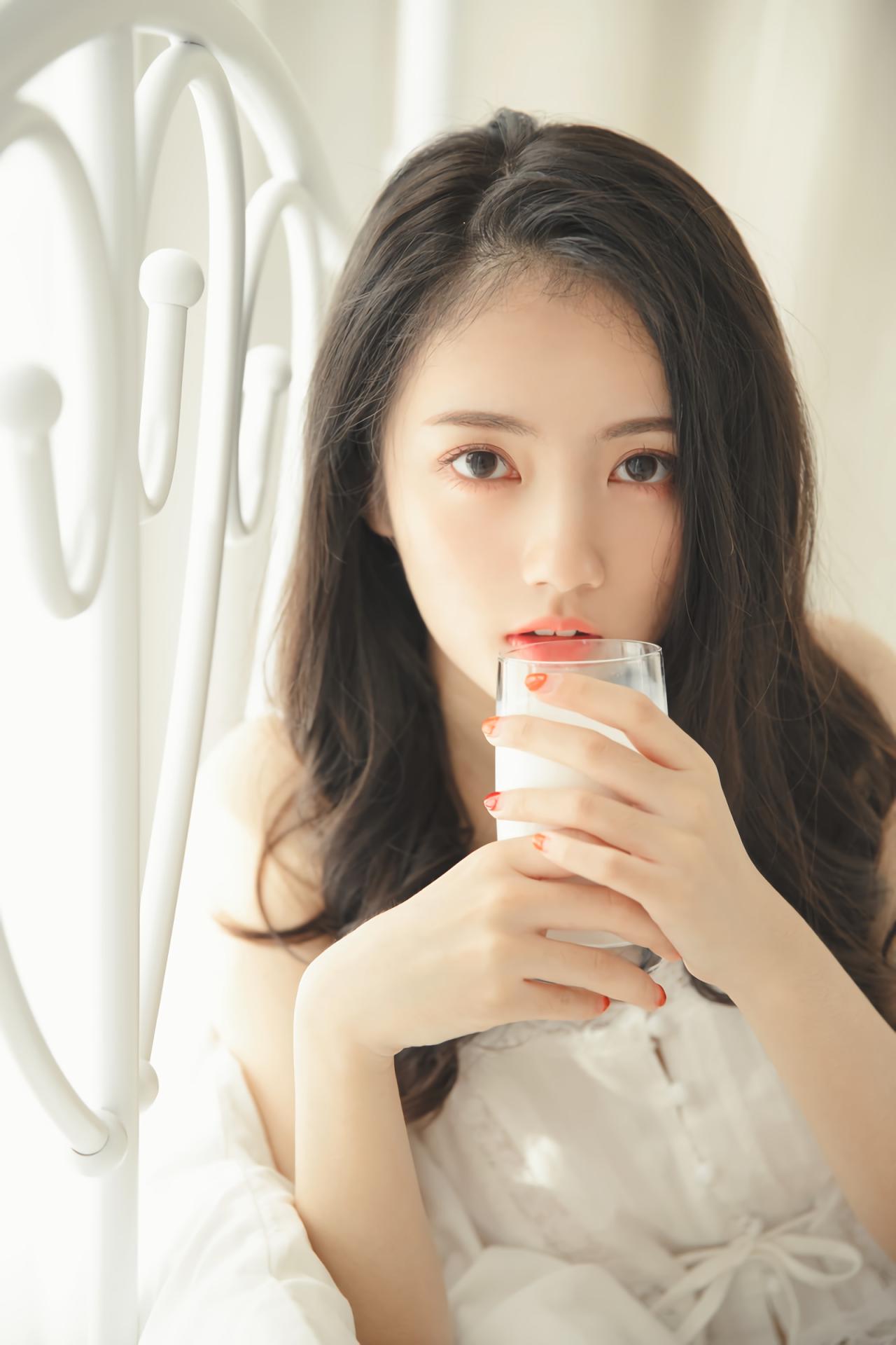 少女双手捧着牛奶，依靠在床上