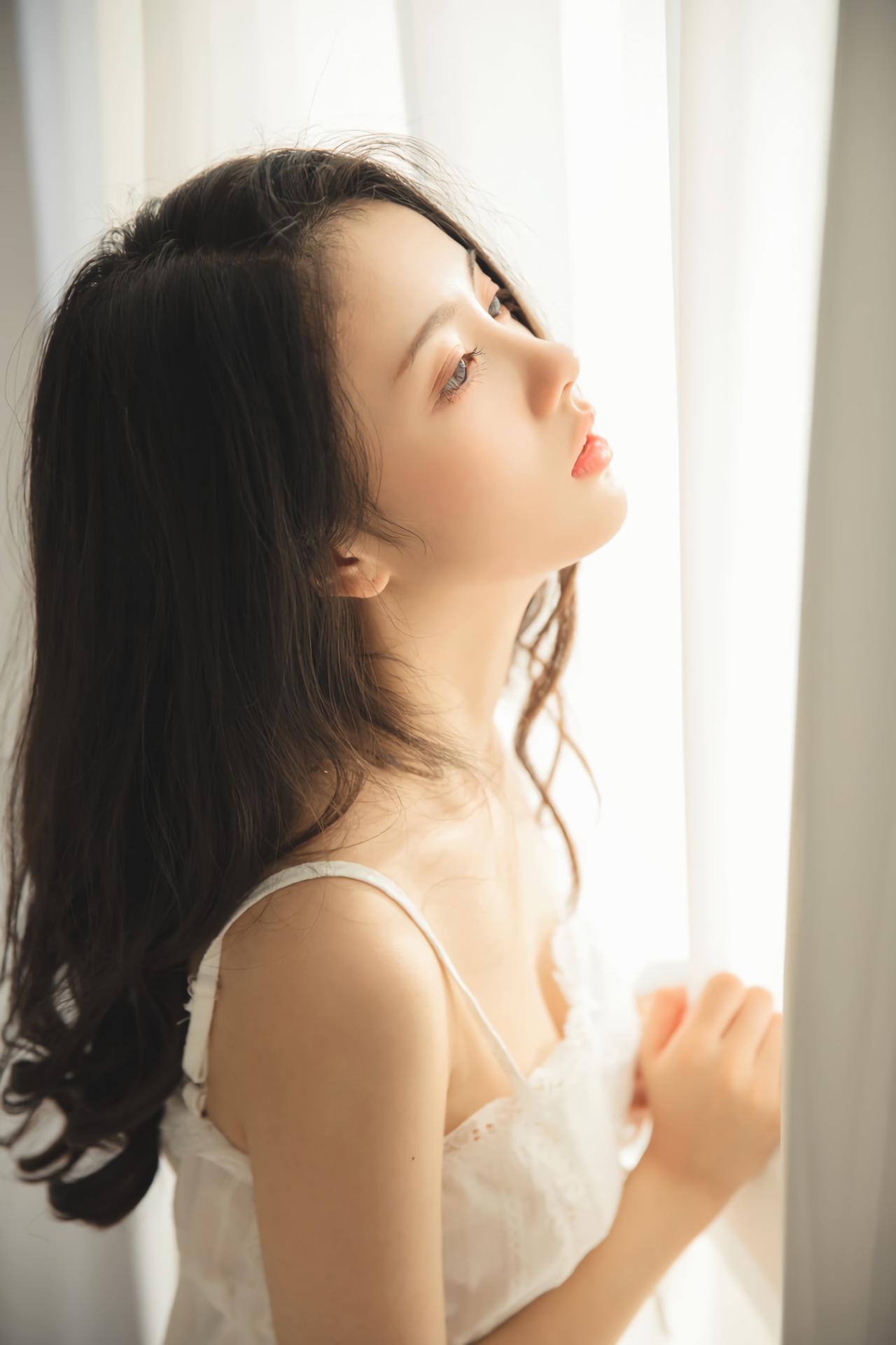 少女侧身站在窗帘前