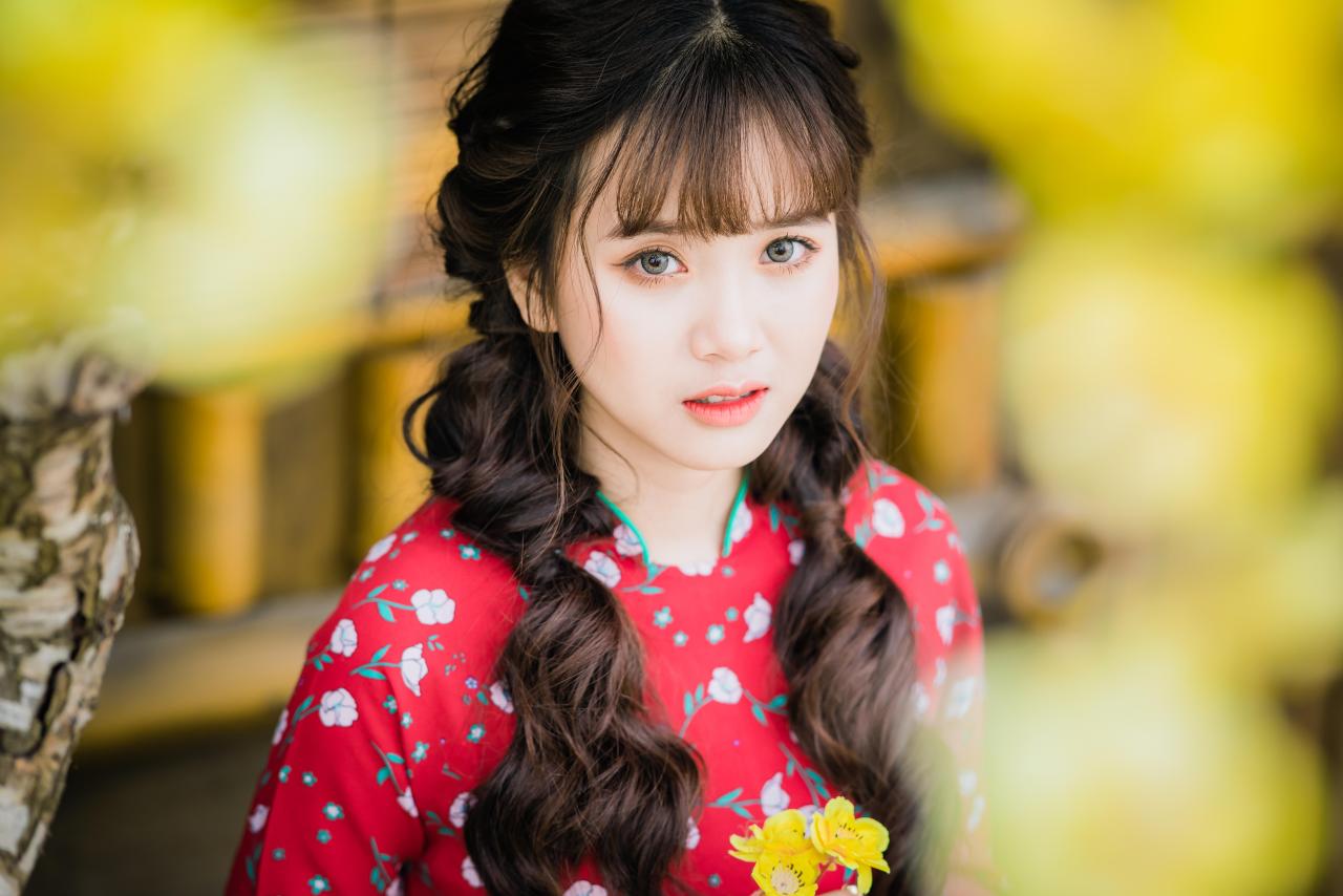 棕色双马尾卷发，齐刘海儿，穿着红色旗袍的越南少女 坐姿 上半身照 4/3 侧面照 横幅 腊梅花 黄梅花 背景虚化